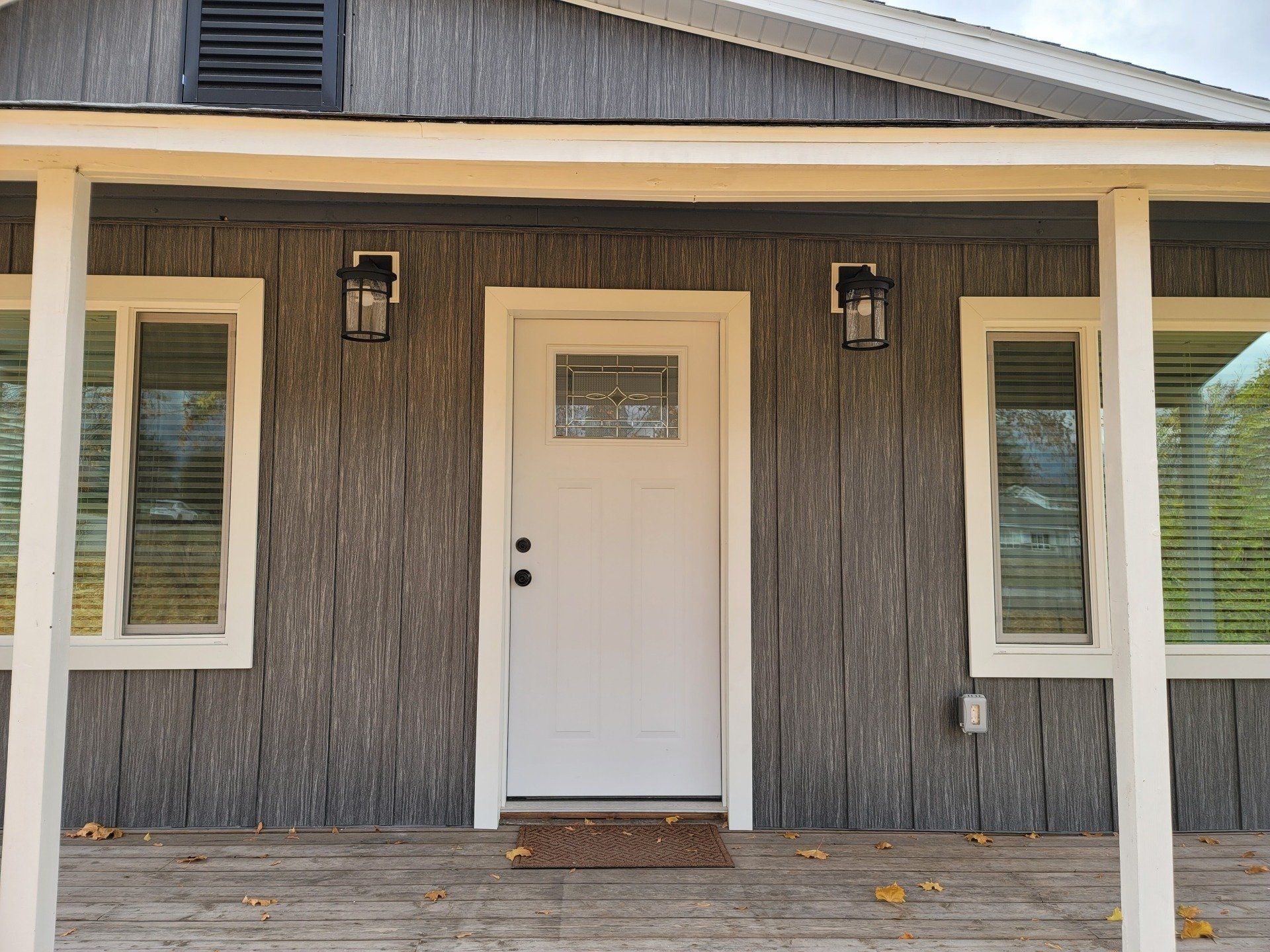 Gray house exterior with white trim, door, and windows. Two black sconces flank the door under a porch.