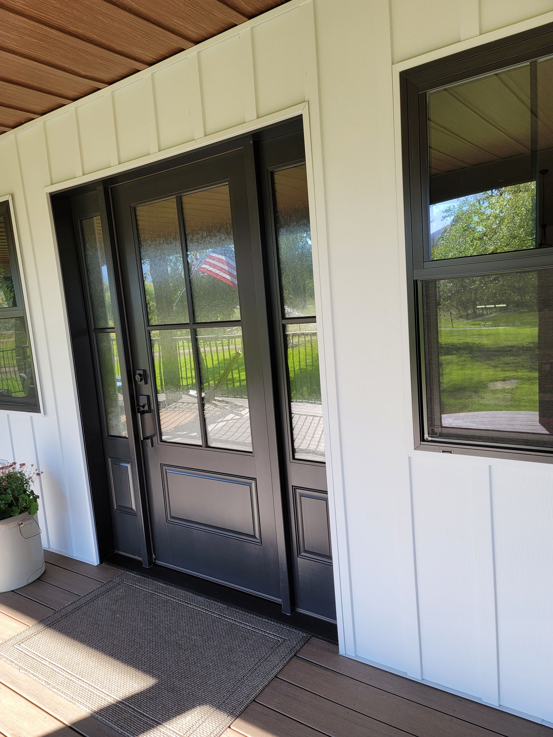 Black door with glass panes, framed in black, on a white siding exterior.