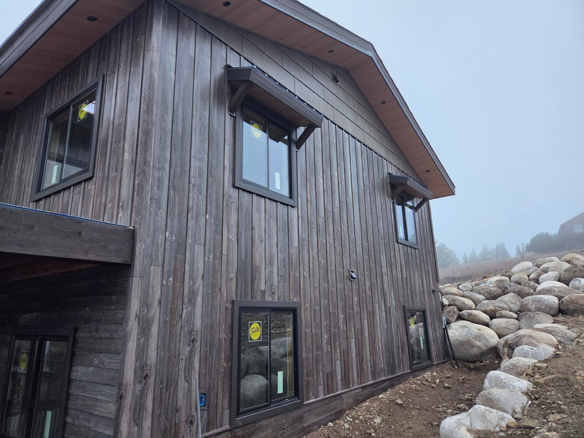 Rustic wooden building with black-framed windows and awnings, set against a foggy hillside.