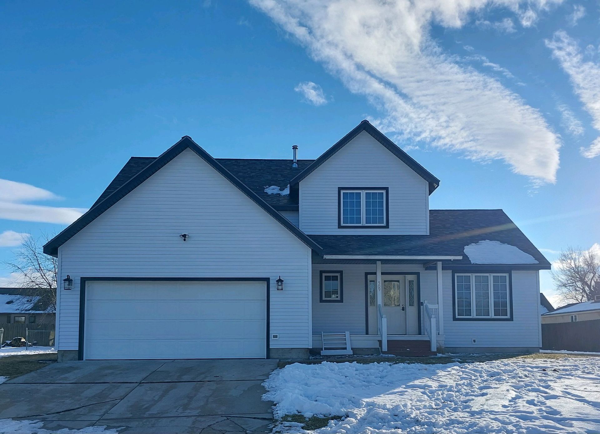 White two-story house with black trim, a two-car garage, and snow on the ground under a blue sky.