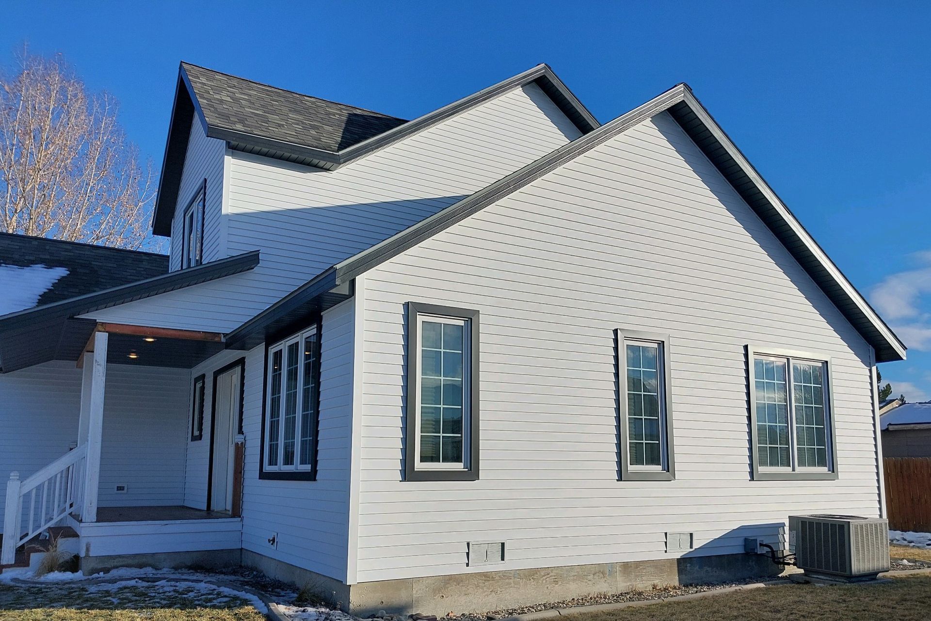 White two-story house with black trim and gray roof against a blue sky.