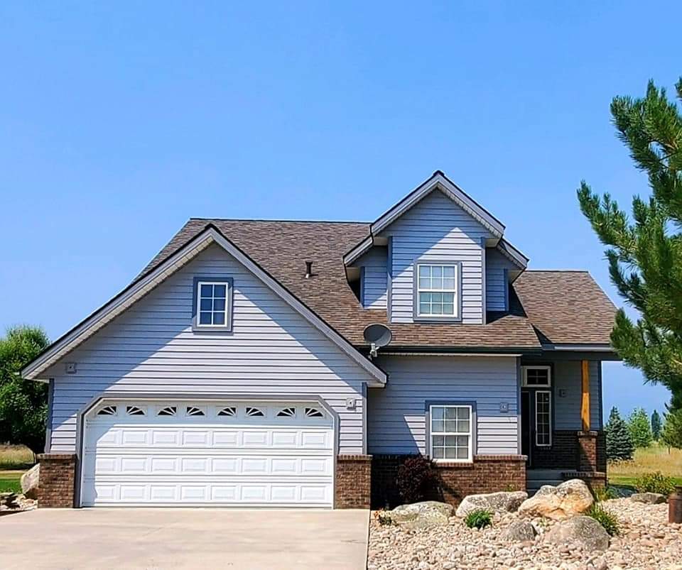 Two-story house with gray siding, a white garage door, and brown roof under a blue sky.