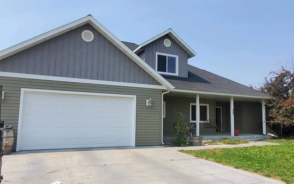 House with gray siding, white garage door, and a porch. Green lawn and a driveway.