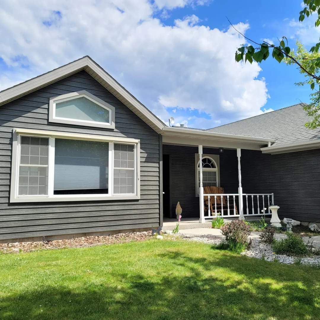 Dark gray house with white trim, porch, and arched window under a cloudy sky.