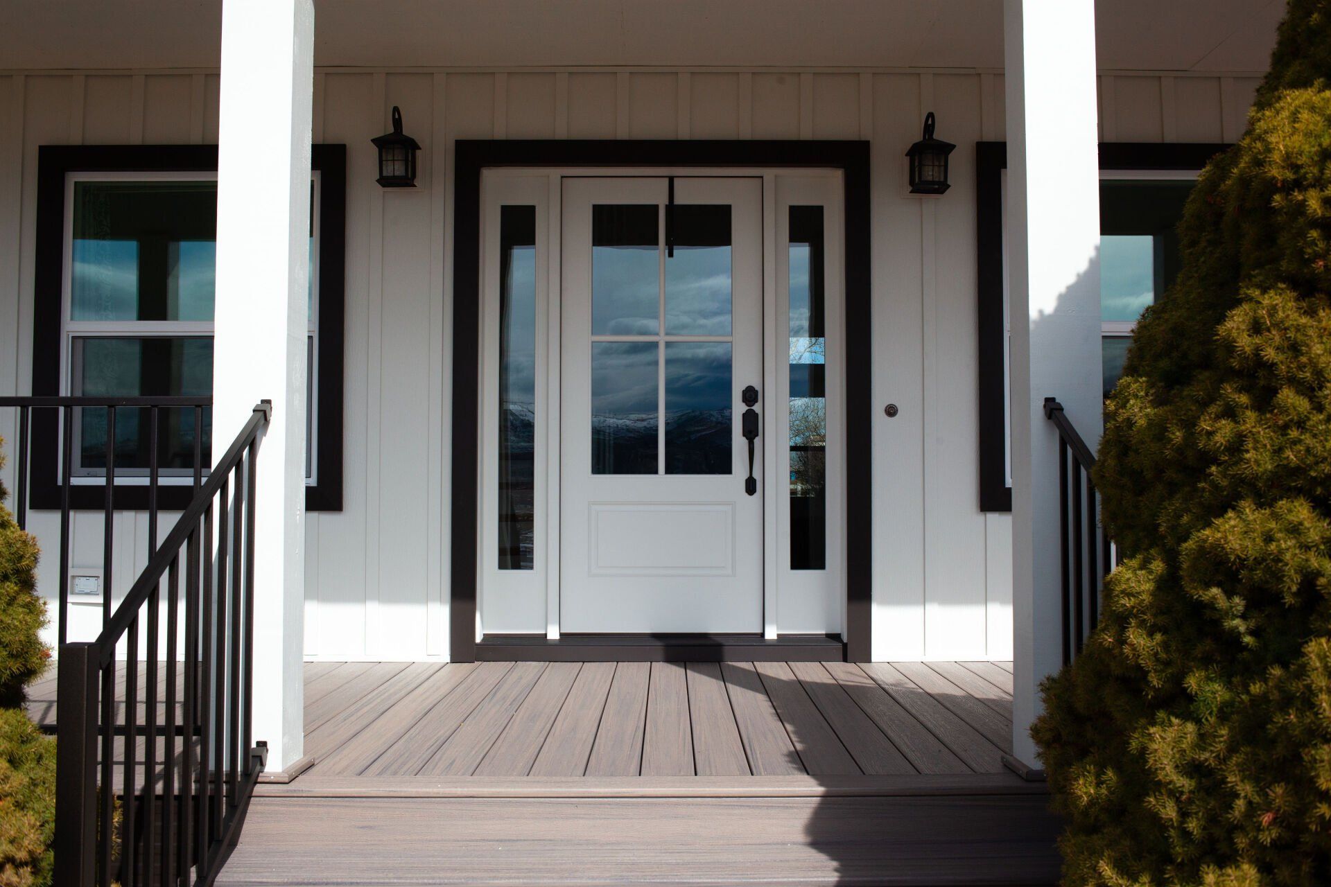 White front door with sidelights, black trim, and small porch under a white overhang.