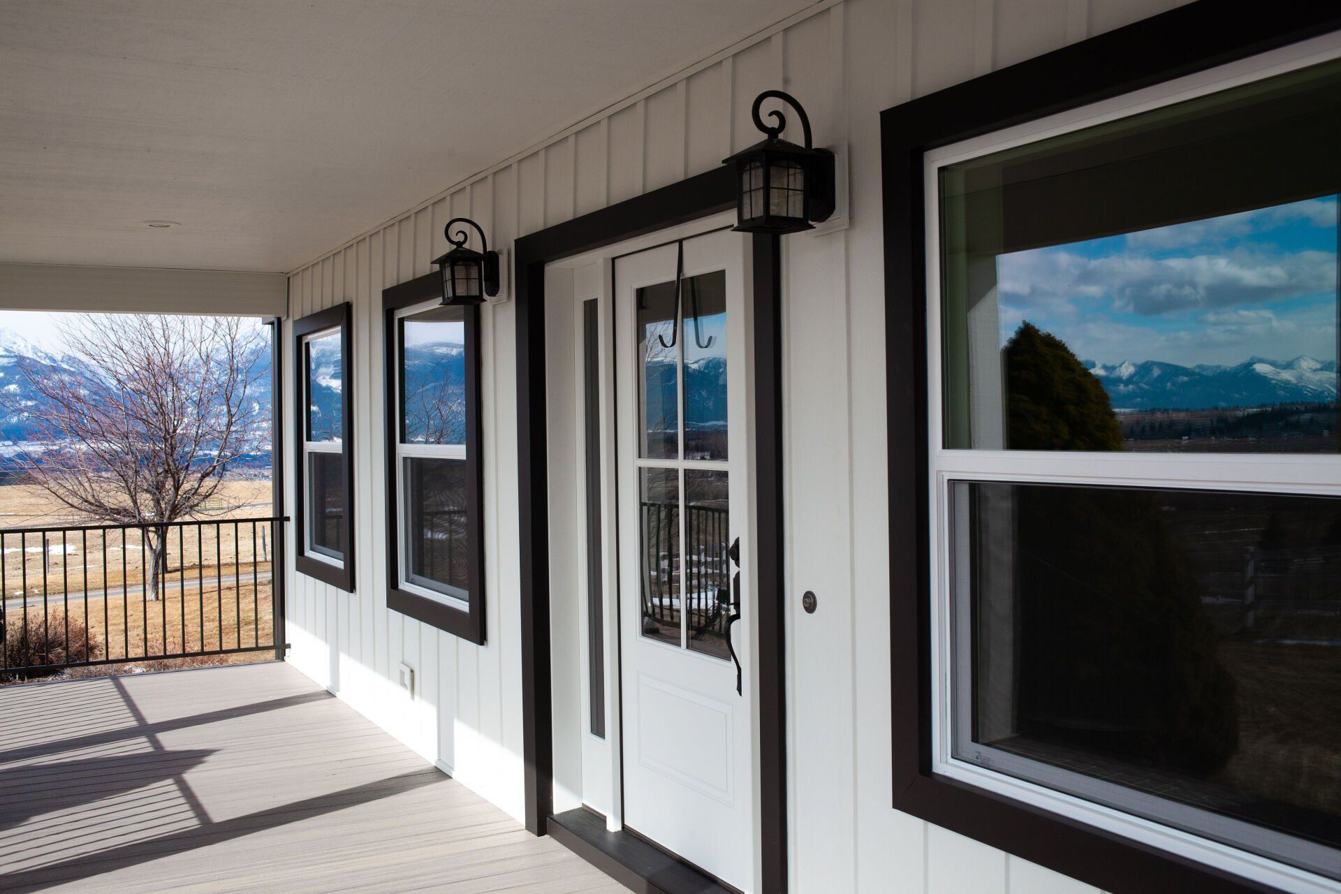White house porch with dark trim, windows, and door. Mountain view in background.