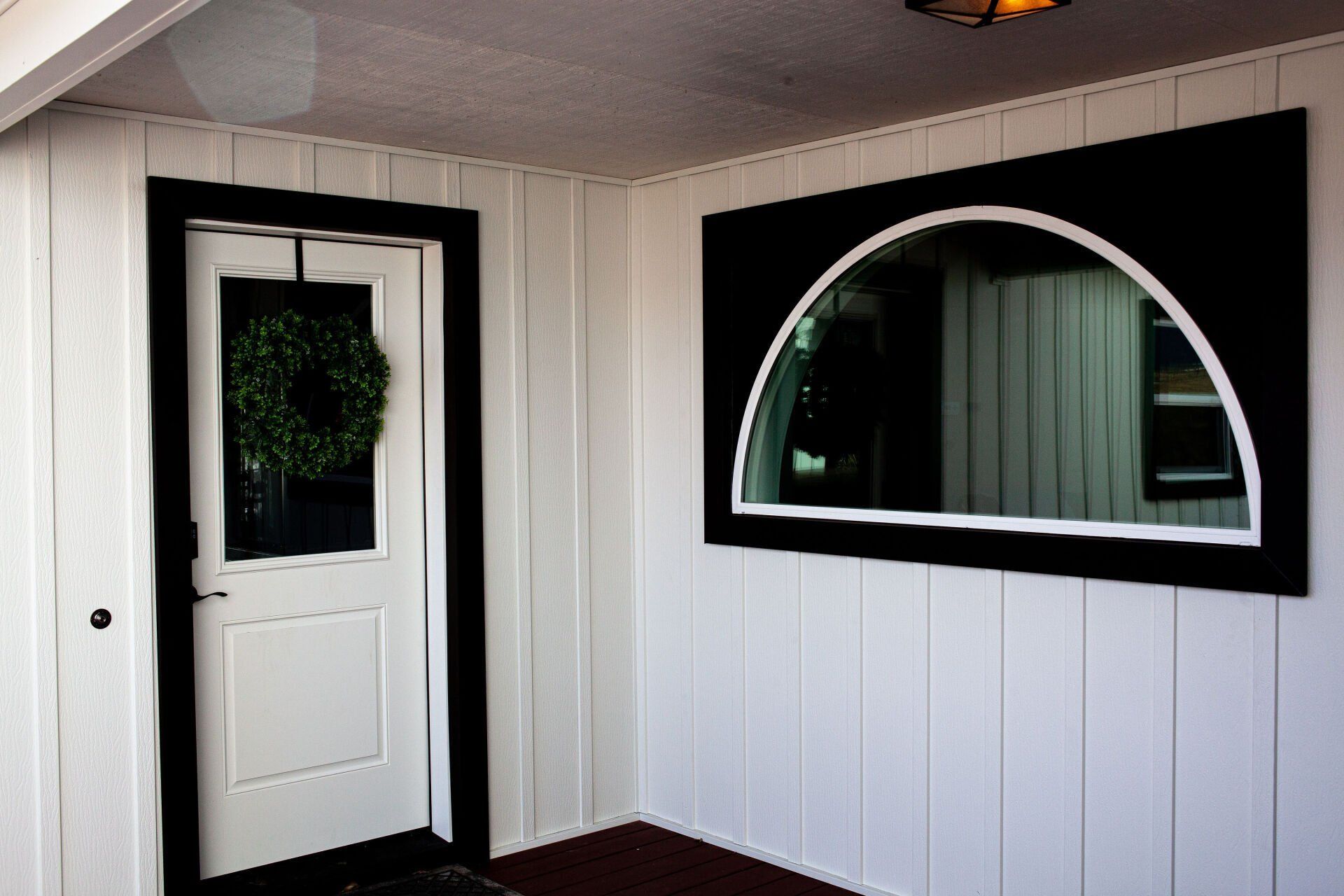 White door with black trim and a wreath, next to a black-framed arched window.