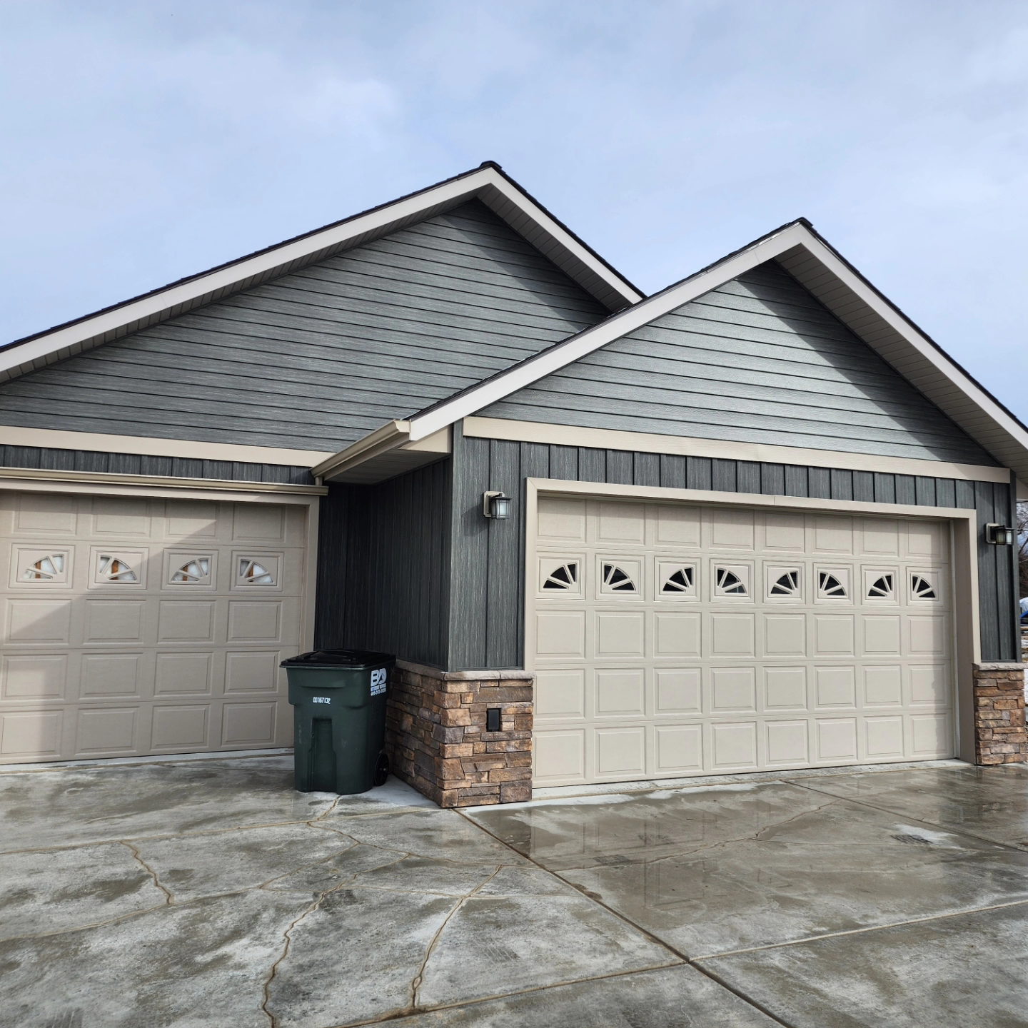 Two-car garage with tan doors and charcoal siding, accented with beige trim and stone.
