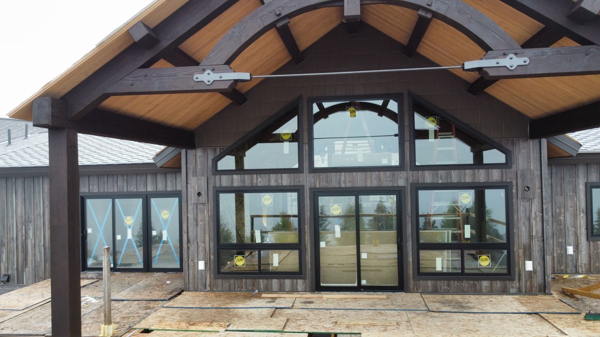 A wooden-clad building with large windows and a covered entrance. Dark wood beams and a brown roof.
