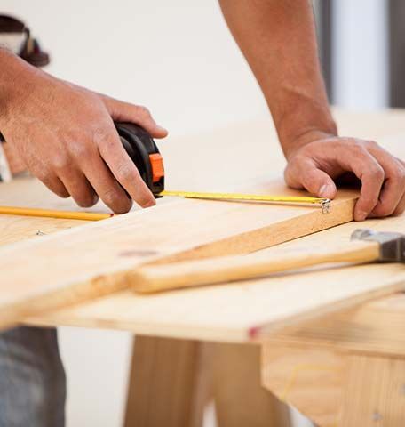 A man is measuring a piece of wood with a tape measure.