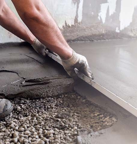 A man is laying concrete on a gravel floor with a trowel.