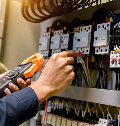 An electrician is working on an electrical panel with a multimeter.