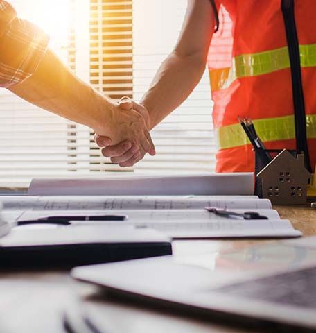 Two construction workers are shaking hands over a table.