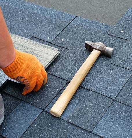 A person wearing orange gloves is working on a roof with a hammer.