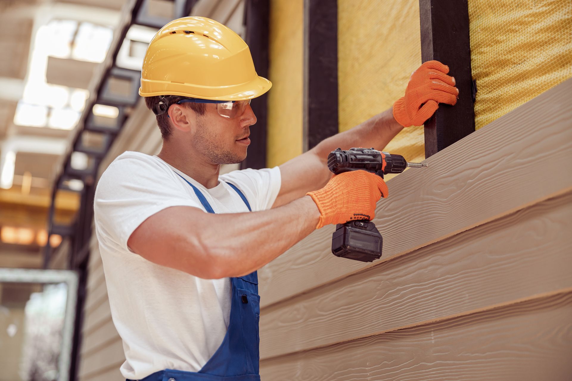 A man wearing a hard hat and gloves is using a drill on a wall.