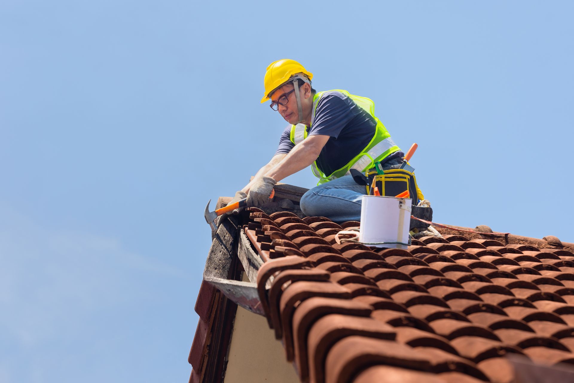 A man is sitting on top of a roof fixing a gutter.