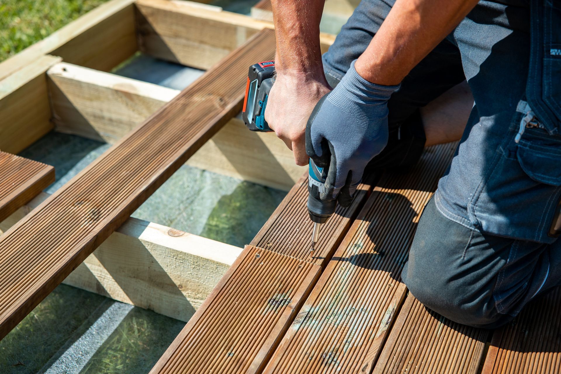 A man is using a drill on a wooden deck.