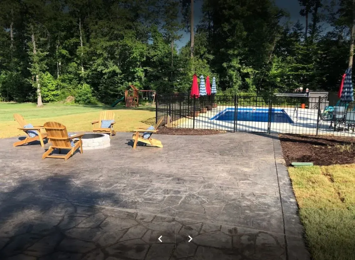 A patio with a fire pit and chairs next to a pool.