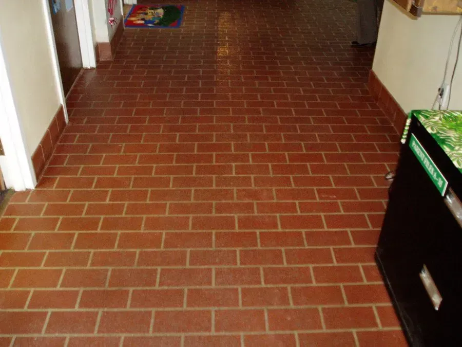 A hallway with a brick floor and a green recycling bin