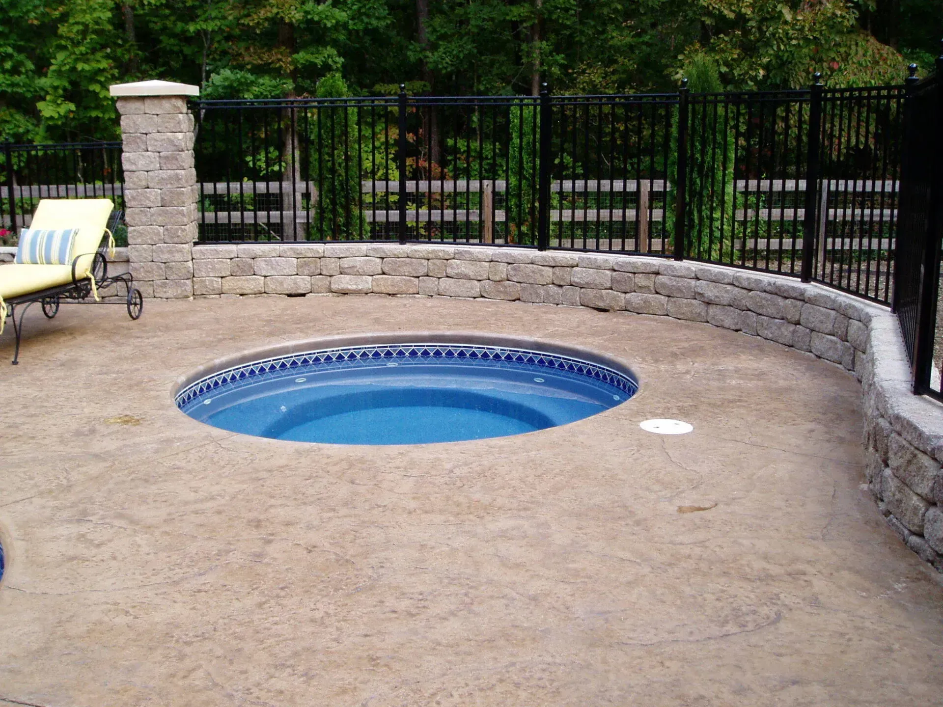 A hot tub is surrounded by a stone wall and a fence