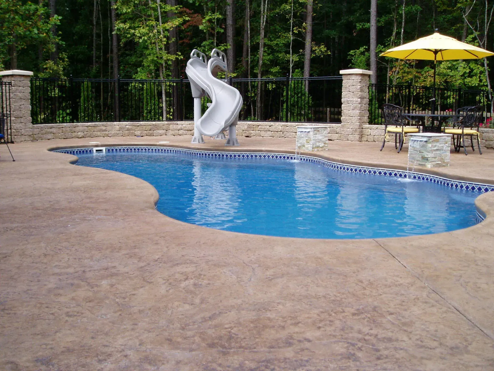 A swimming pool with a slide and a yellow umbrella