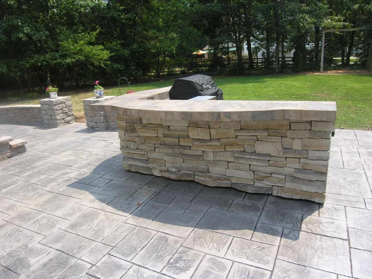 A large stone wall is sitting on a patio next to a grill.