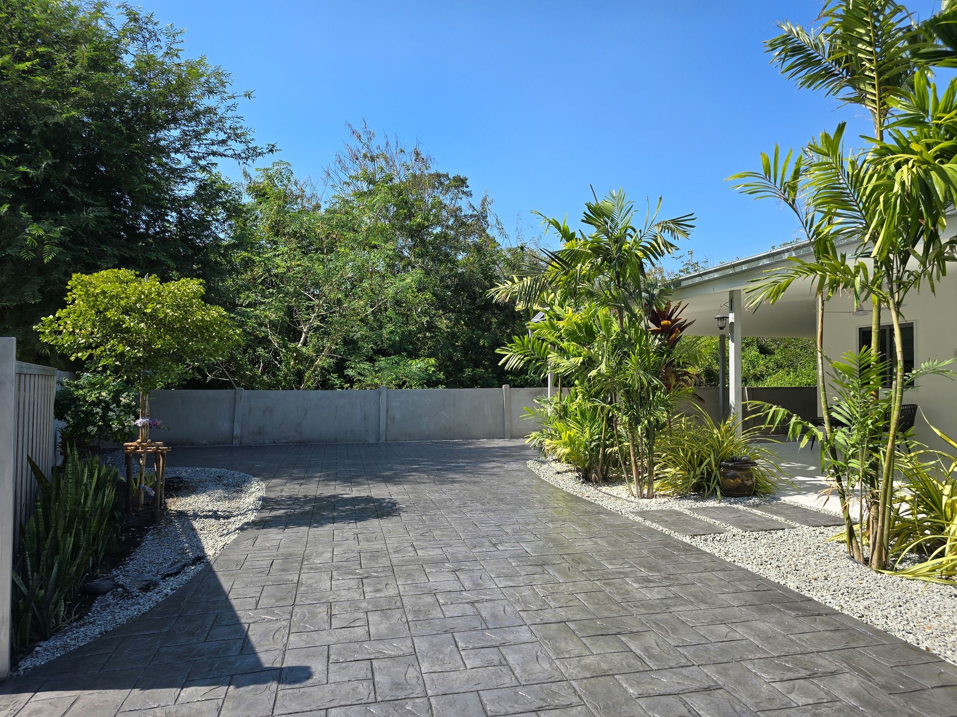 Driveway with stamped concrete, lined with trees and plants, leading to a house.