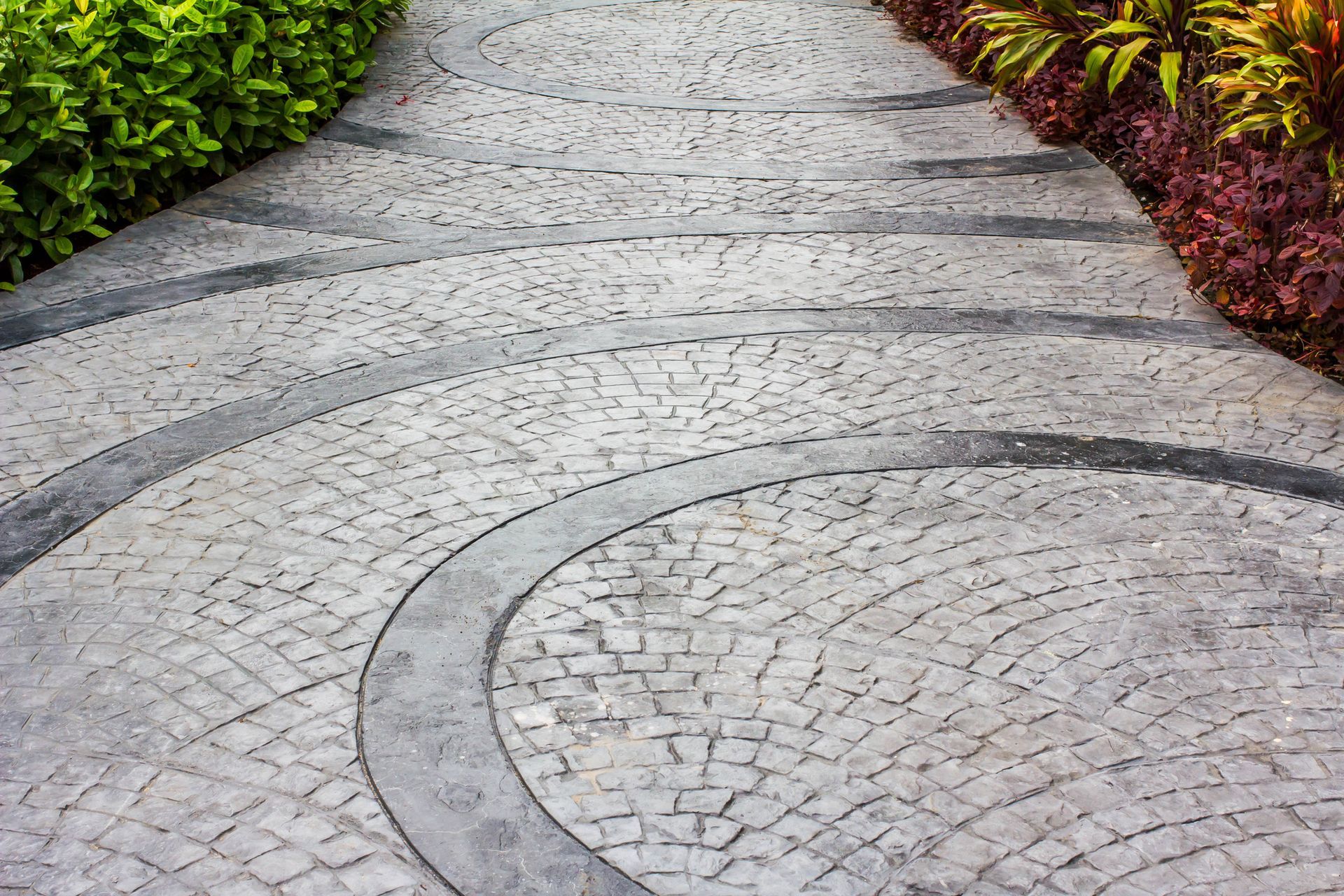 A brick walkway with a circular design in the middle of a garden