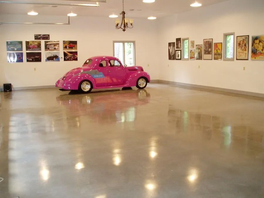 A pink car is parked in a garage with pictures on the wall