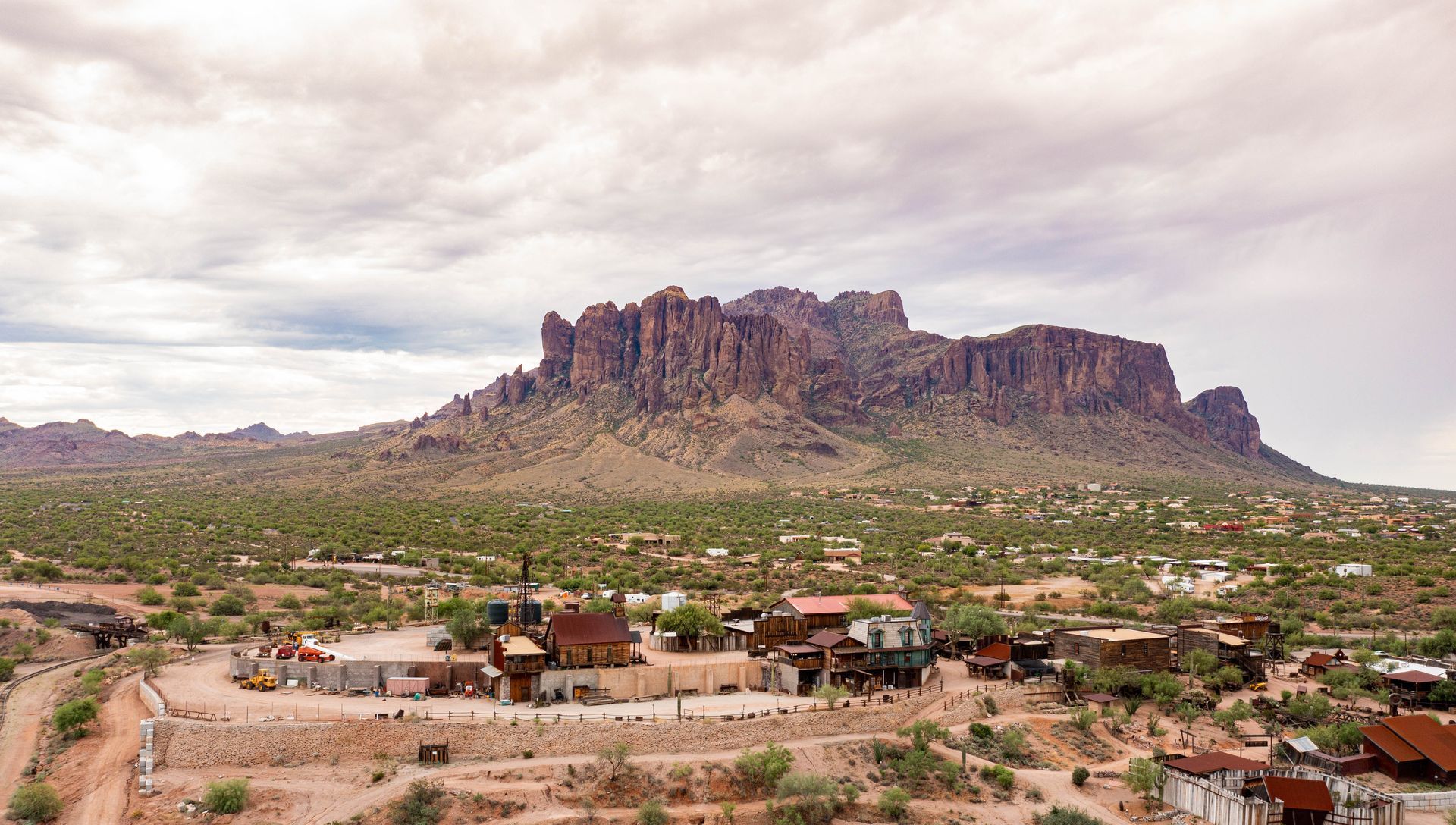 Desert town beneath a rugged mountain ridge under cloudy skies