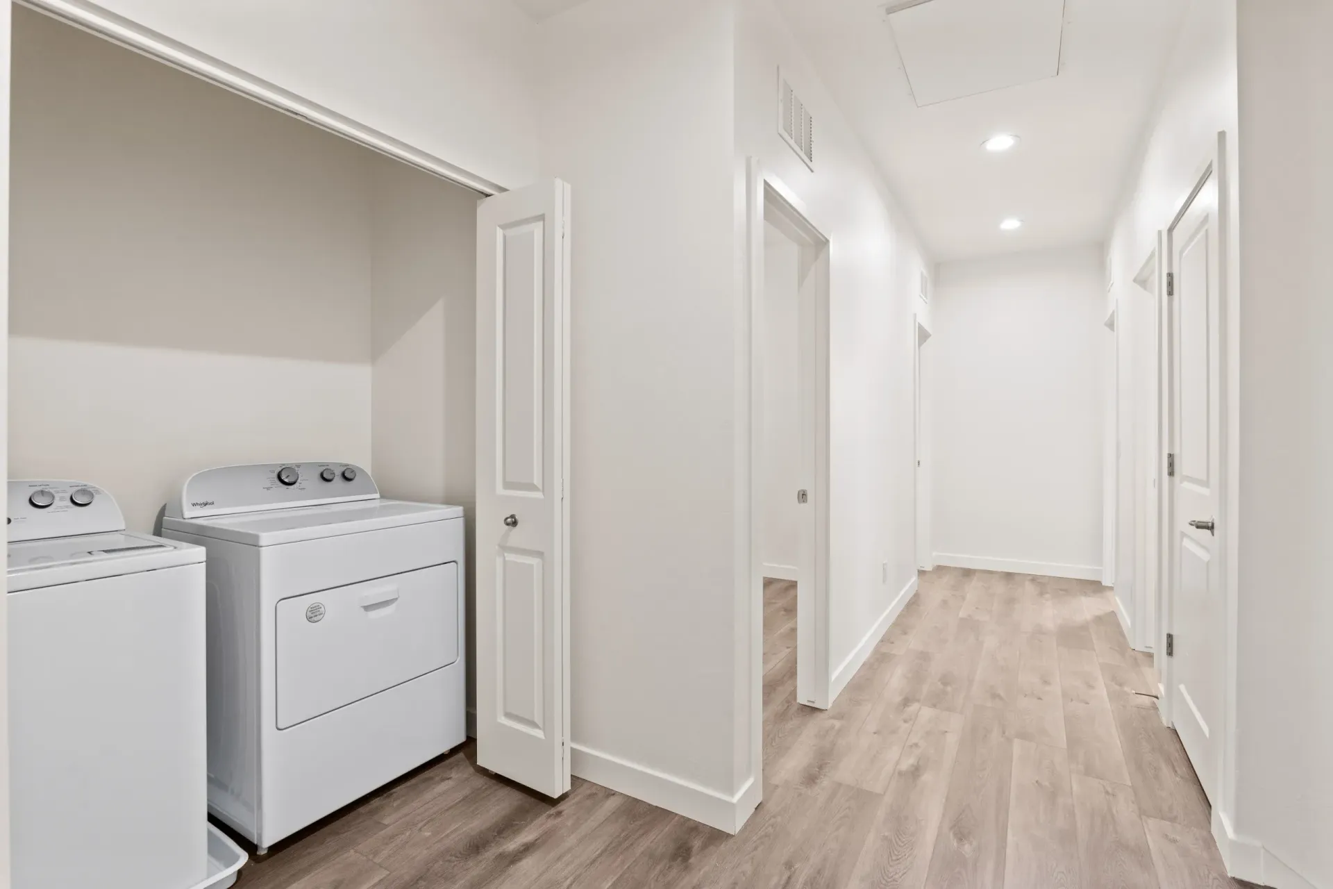 Bright laundry room and white hallway with wood floors and open closets