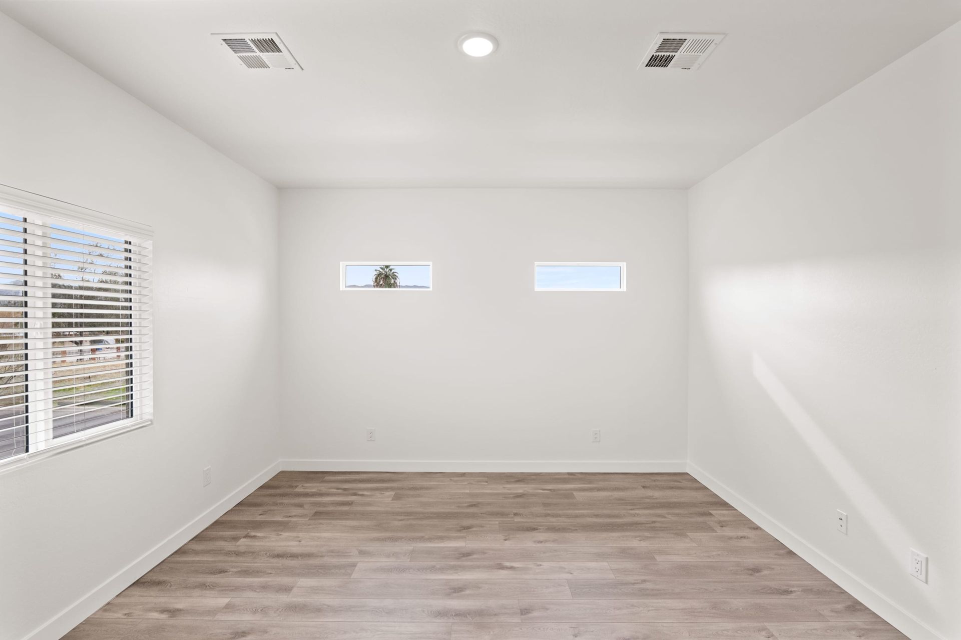 Empty white room with wood-look floor and two small windows on the far wall.