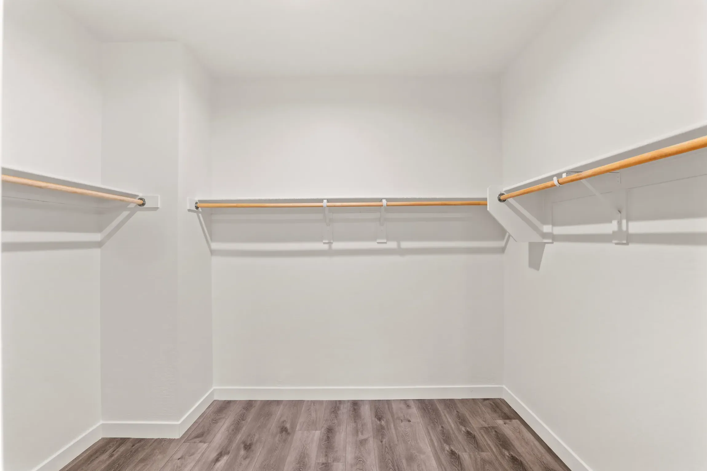 Empty walk-in closet with white walls, wood shelves, and gray wood-look flooring.