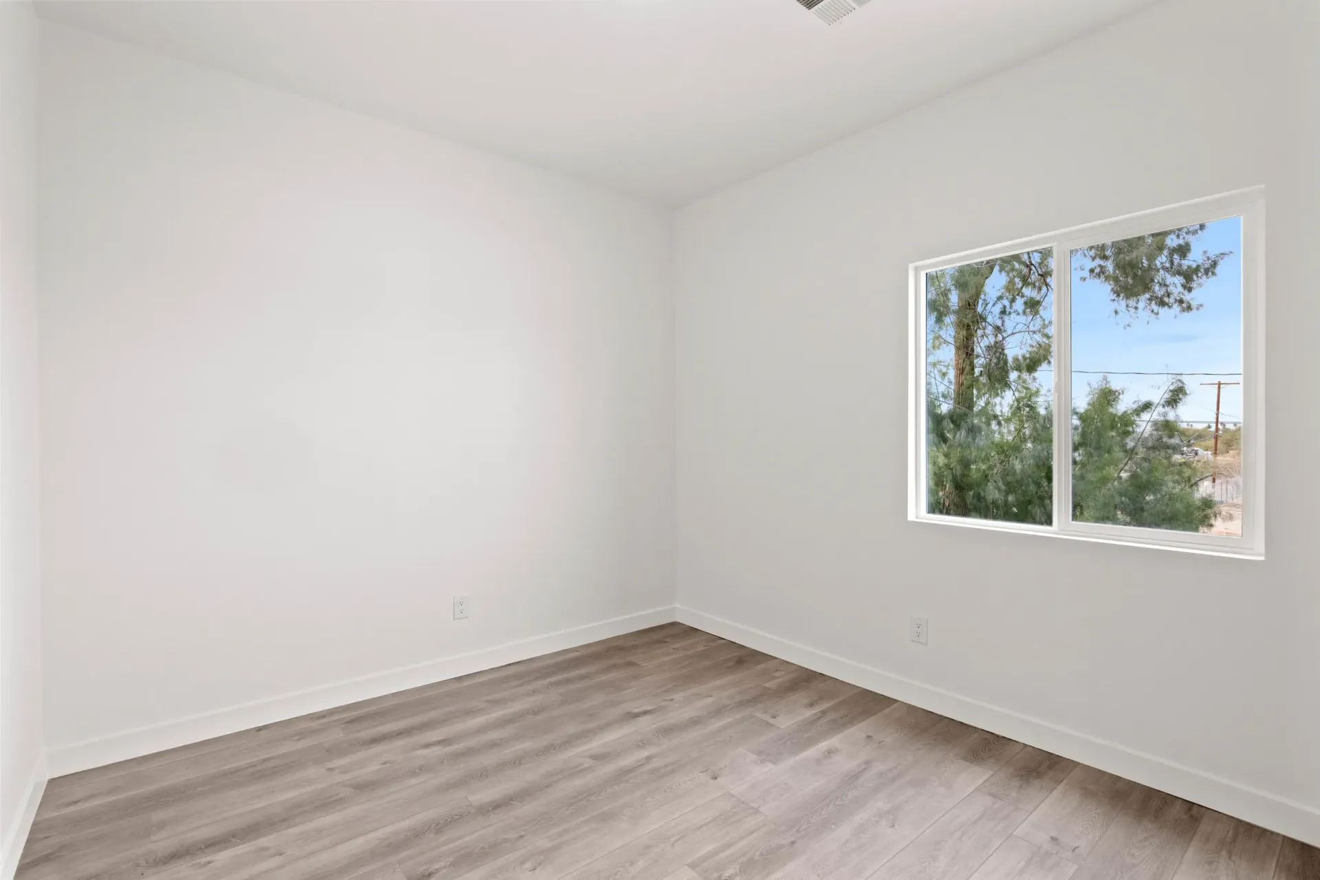 Empty white room with light wood flooring and a window showing trees outside