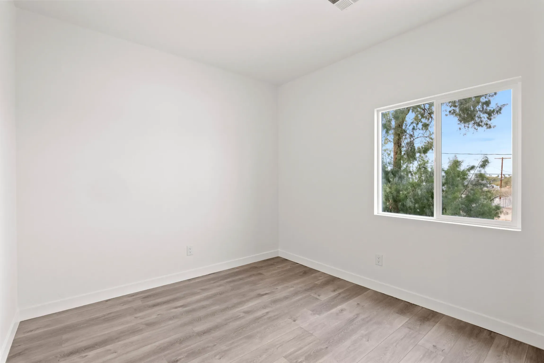 Empty white room with light wood flooring and a window showing trees outside