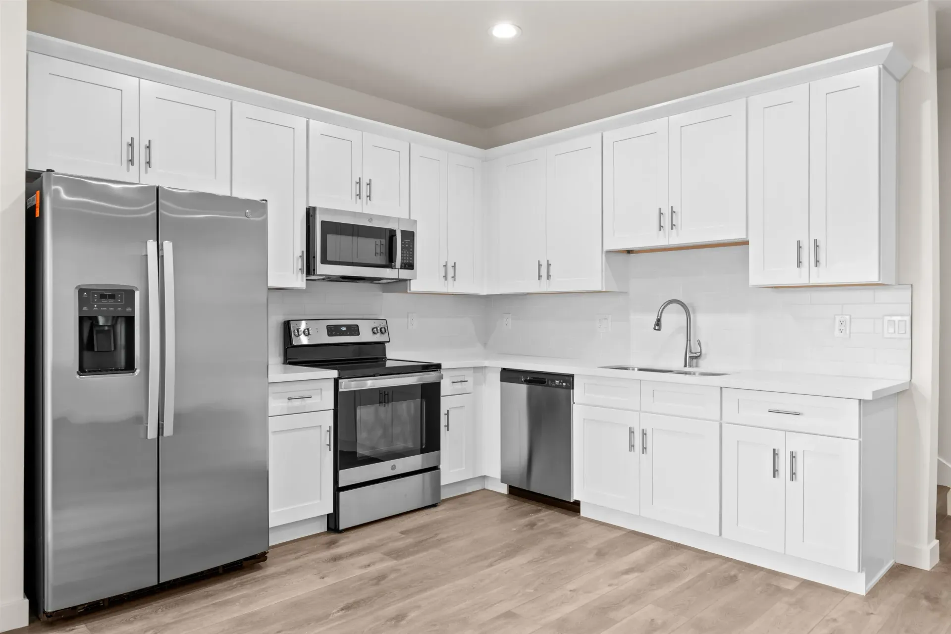 Bright white modern kitchen with stainless steel appliances and light wood flooring
