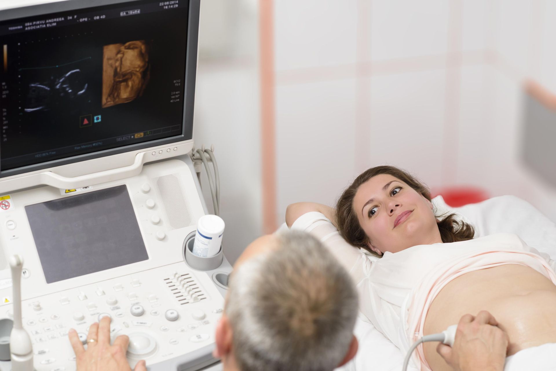 Woman getting an ultrasound scan, doctor examining abdomen with monitor displaying images in a medical office.