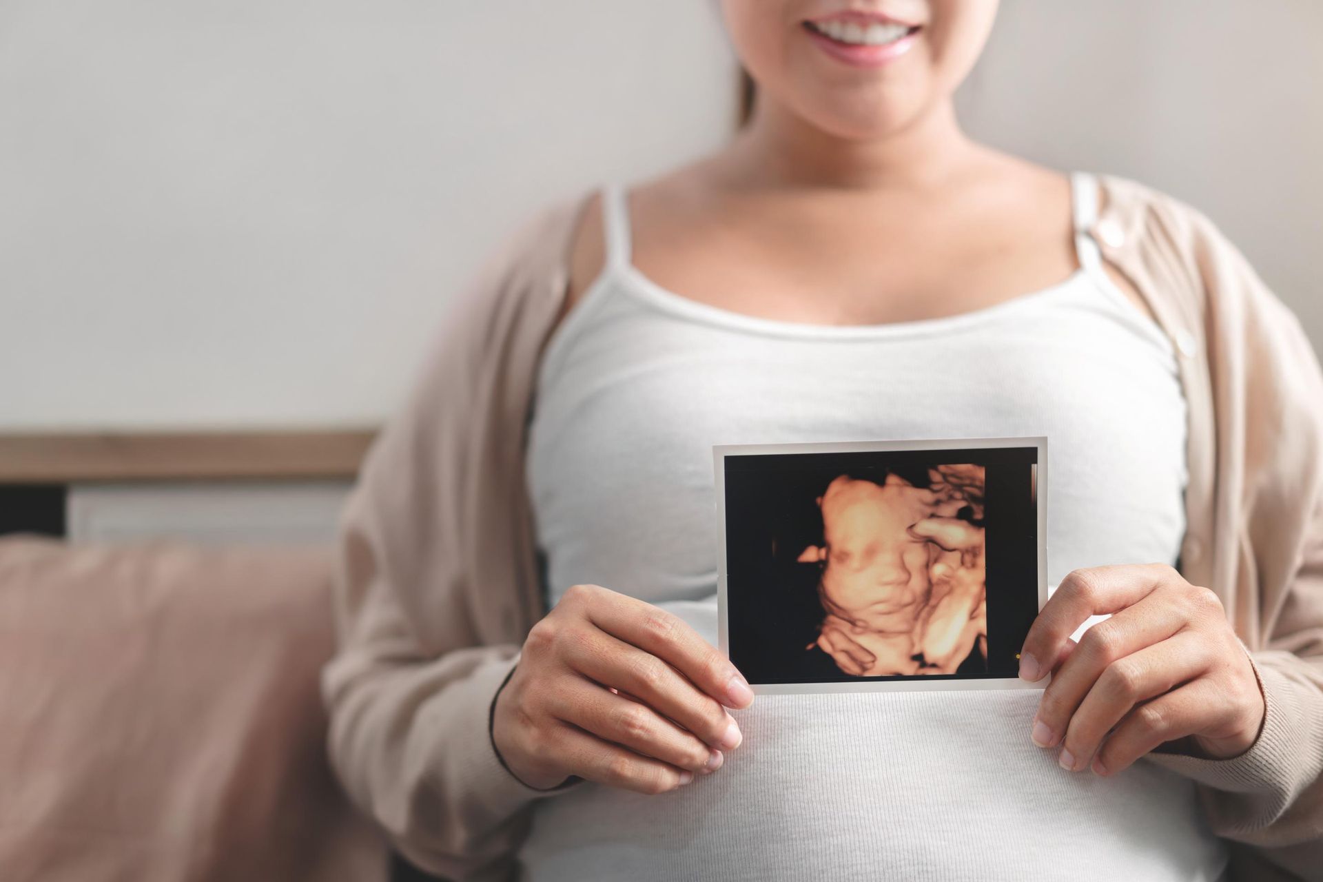 Pregnant woman smiling, holding ultrasound picture of her baby.