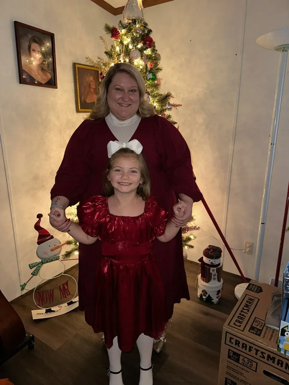 Woman and child in red outfits stand in front of a decorated Christmas tree.