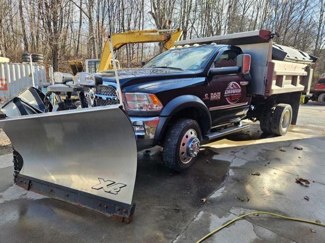 Aerial view of a person standing on dirt near a small yellow excavator in a partially landscaped yard with trees.