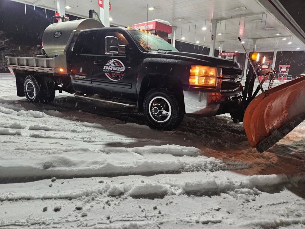 A dark-colored pickup truck with a large orange snowplow attached to the front parked in the snow at night.