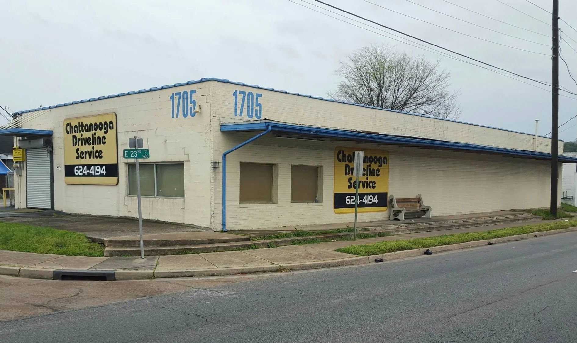 Corner storefront with blue awning and signs on a quiet street under an overcast sky