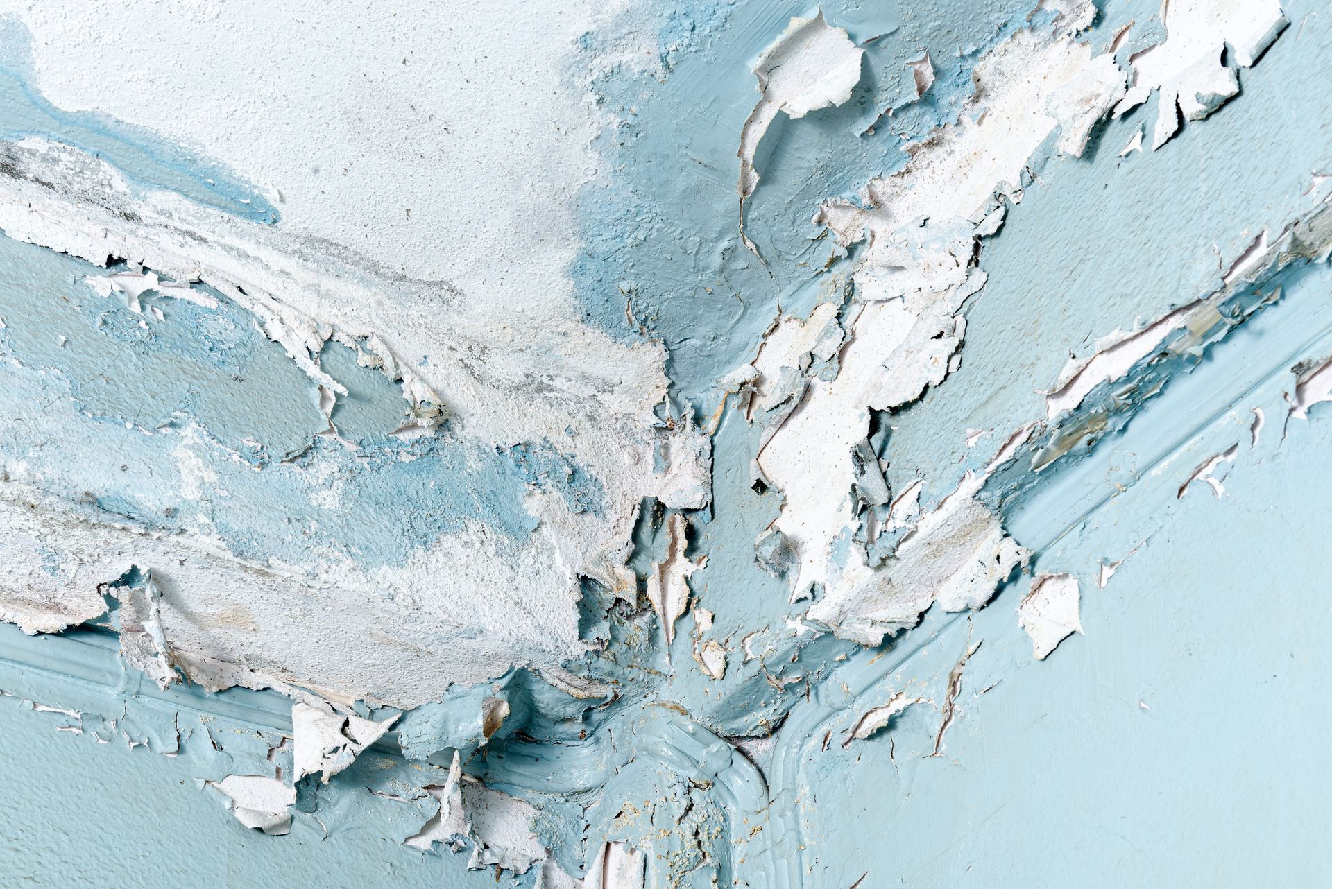 Peeling blue and white paint at ceiling corner with moisture damage.