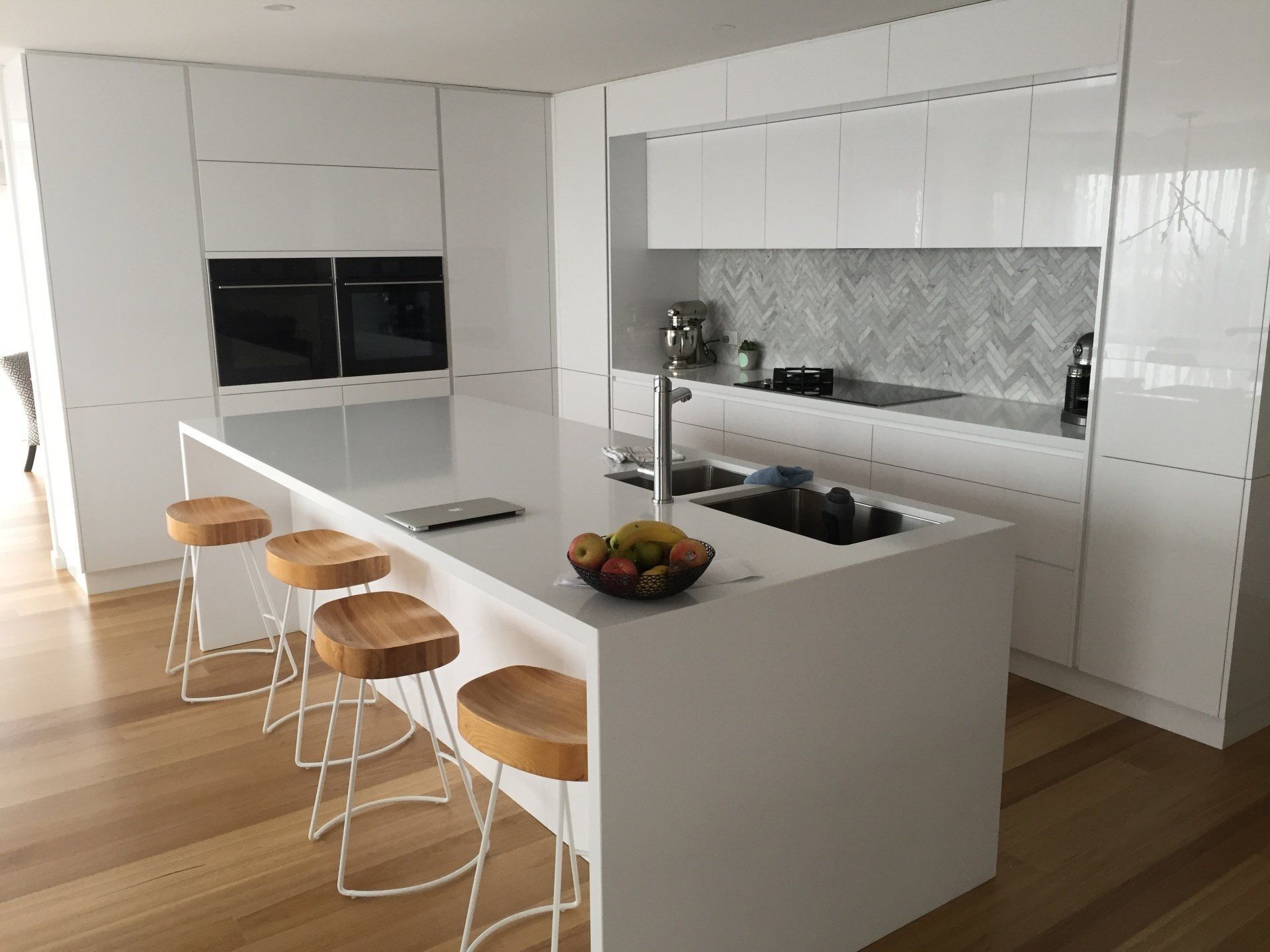 A kitchen with a large island and stools and a bowl of fruit on the counter.