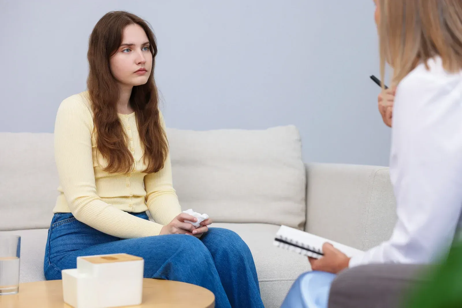 A person in a yellow top talks to a professional holding a notebook in a calm office setting.