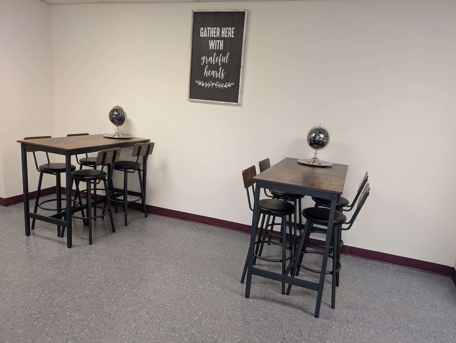 Two dark wood high-top tables with black stools and decorative globes sit in a room with a framed wall sign.