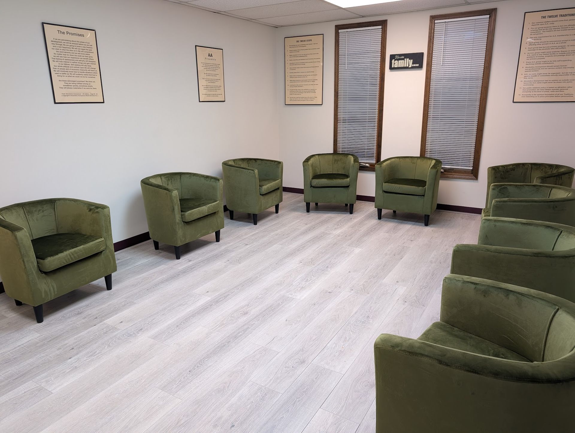 A room featuring a circle of olive green armchairs arranged on a light wood floor, with framed prints on the walls.