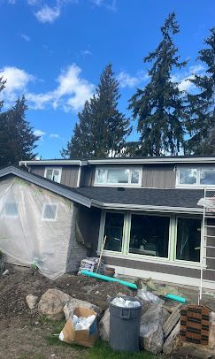 House exterior under construction with gray siding, blue sky, and trees.