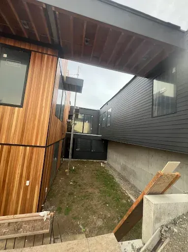 Exterior view of modern house under construction with wooden siding and a dark gray roof.