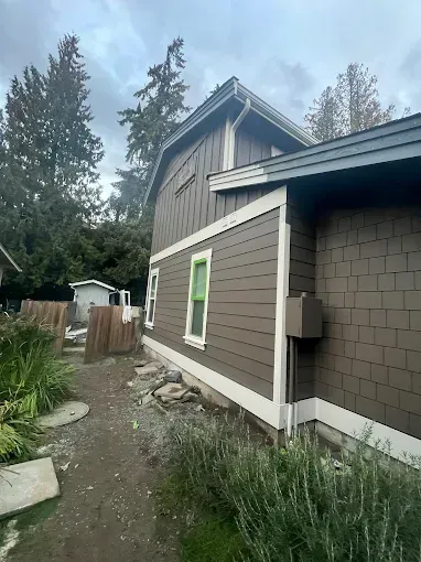 Brown house with white trim, green-framed windows, and a blue roof under an overcast sky.